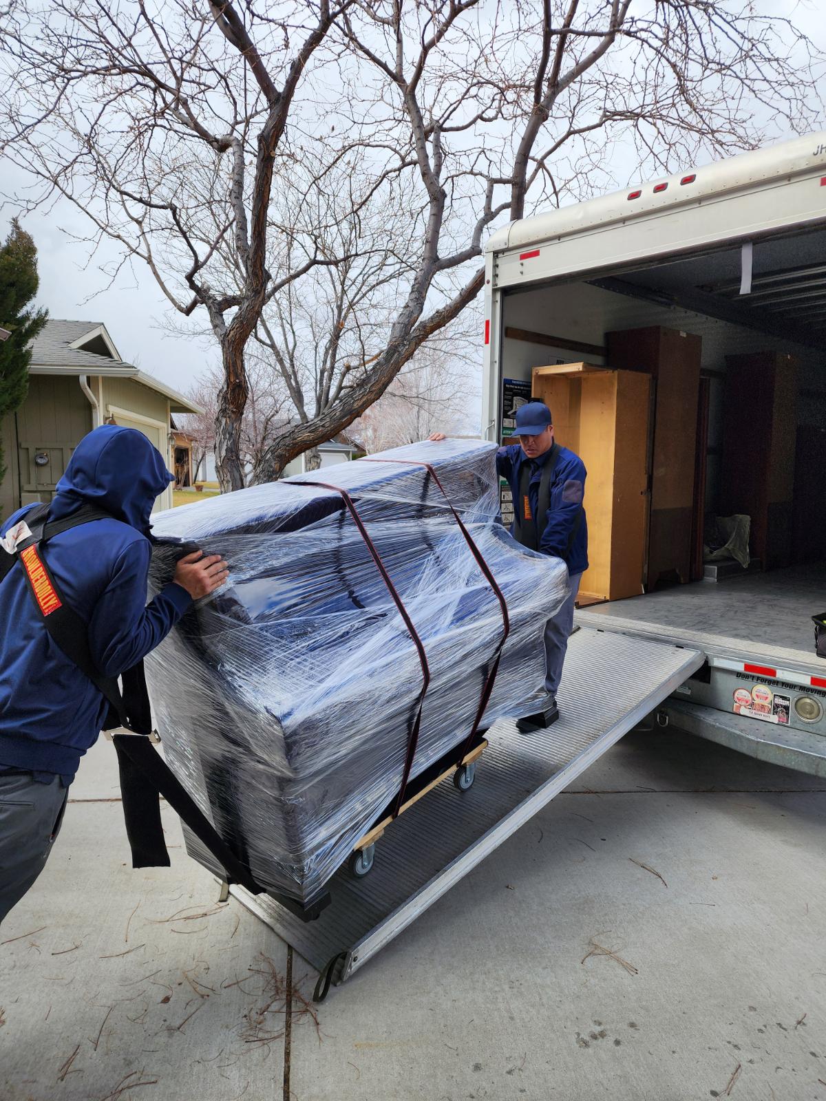 Green Echo movers loading a wrapped piano onto a moving truck ramp