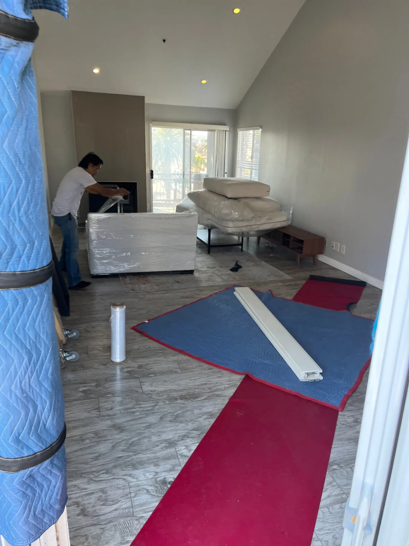 Green Echo mover shrink-wrapping a sofa in an Orange County living room with floor runners laid down